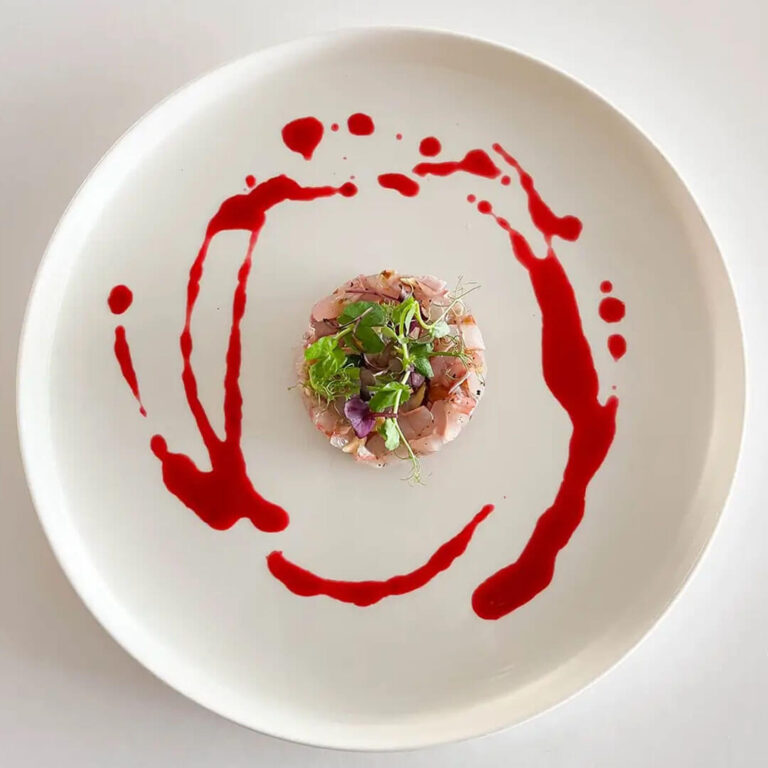 Battuta di pesce crudo con erbe fresche e decorazione di salsa rossa
