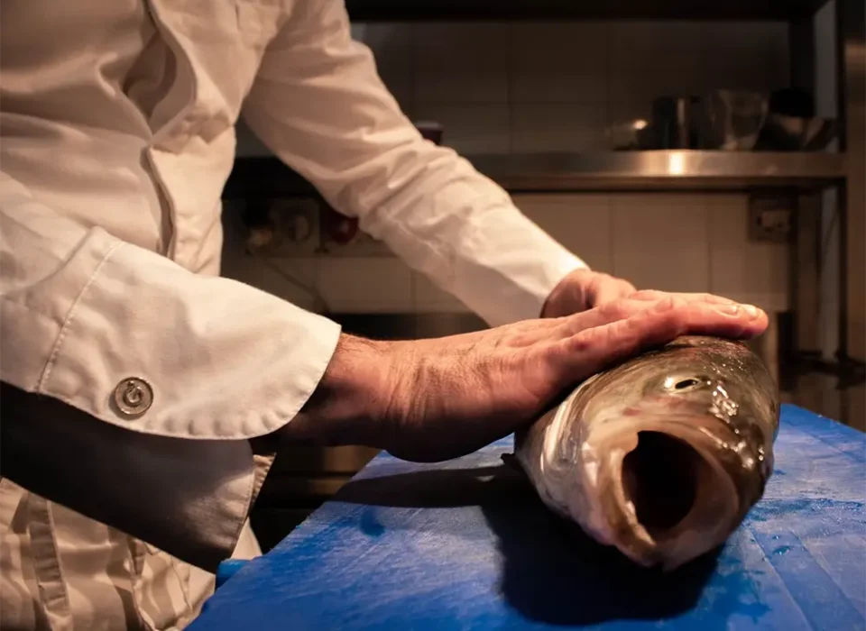 Lo chef seleziona un pesce fresco intero sul tagliere nella cucina del bistrot
